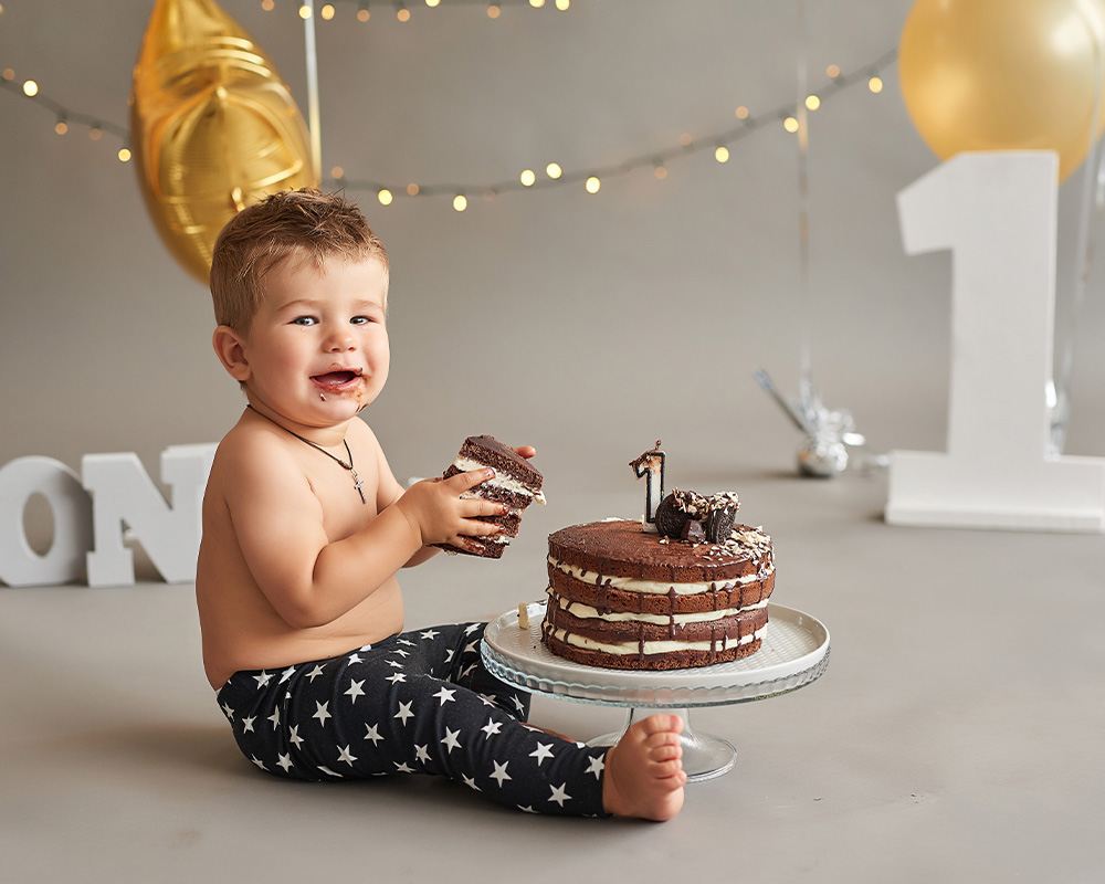 Jednogodišnji dječak drži komad čokoladne torte u rukama kako bi proslavio svoj rođendan