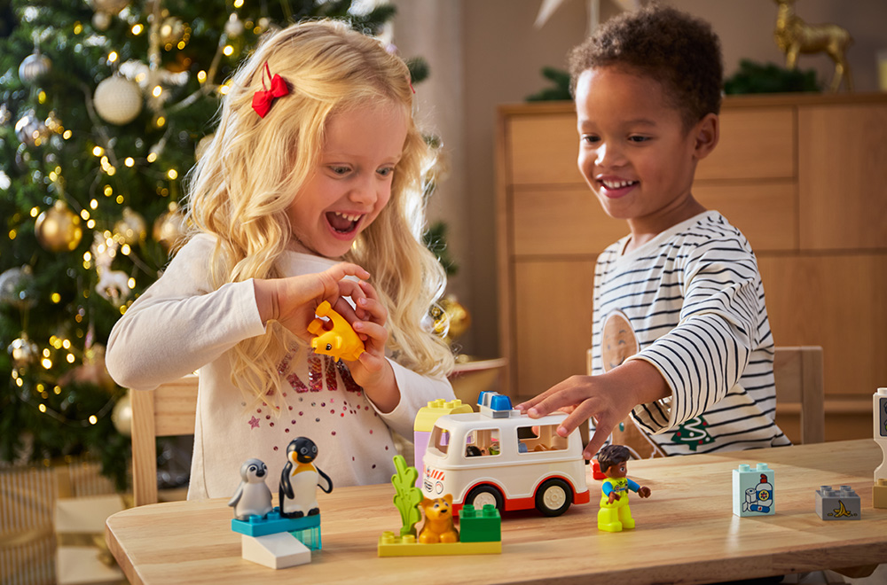 Dvoje djece se igra LEGO kockicama ispod jelke.