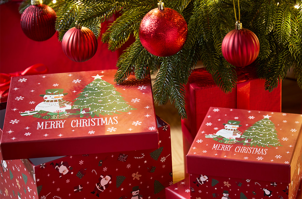 Poklon kutije s božićnim motivima pored jelke.