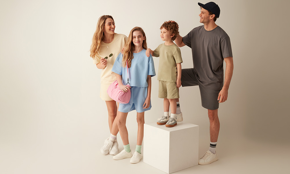 Porodica u pastelnim odjevnim kombinacijama pozira zajedno na svijetloj pozadini.